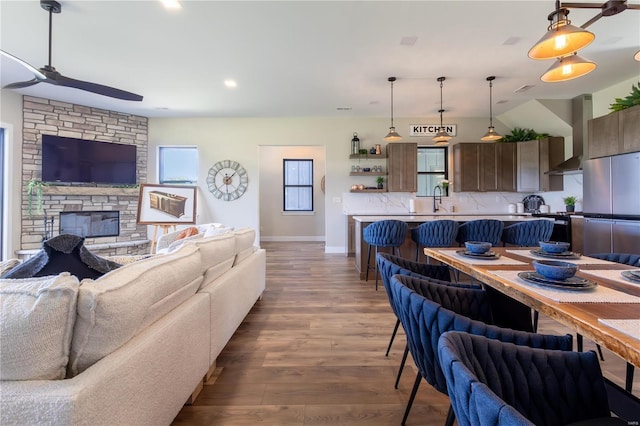 living room with sink, ceiling fan, dark hardwood / wood-style flooring, a stone fireplace, and vaulted ceiling