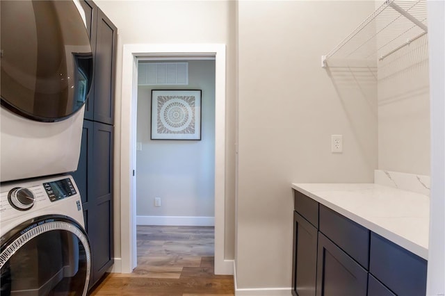 laundry area with cabinets, stacked washer and dryer, and light hardwood / wood-style flooring