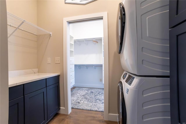 laundry area featuring cabinets, stacked washer / drying machine, and dark hardwood / wood-style floors