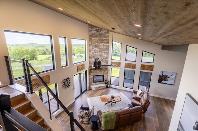 living room with wood ceiling, a towering ceiling, wood-type flooring, and a stone fireplace