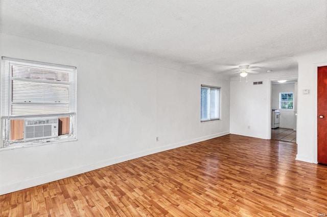 empty room with cooling unit, ceiling fan, light hardwood / wood-style floors, and a textured ceiling