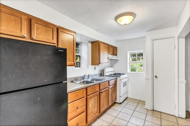 kitchen featuring light tile patterned flooring, black refrigerator, sink, and white gas range oven