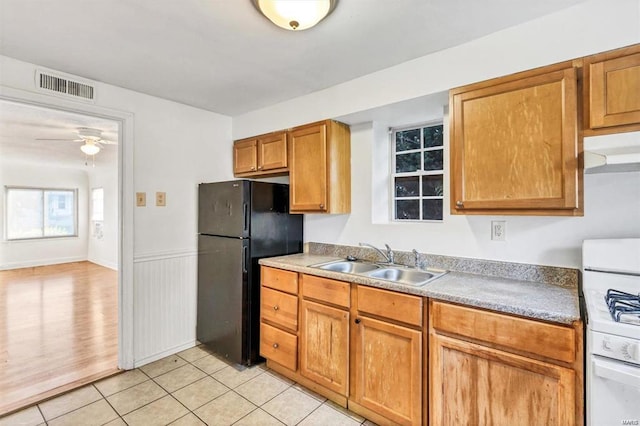 kitchen with white gas stove, sink, light tile patterned floors, black refrigerator, and ceiling fan