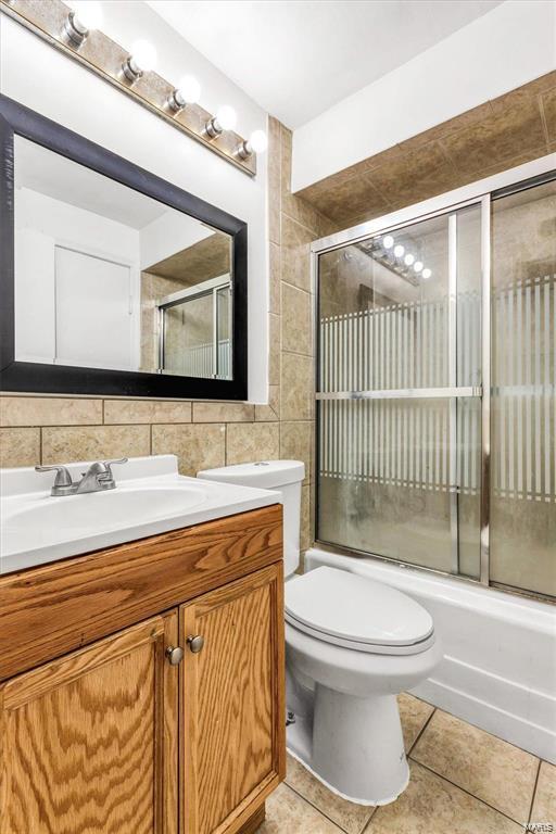 full bathroom with combined bath / shower with glass door, tile walls, vanity, toilet, and tile patterned floors