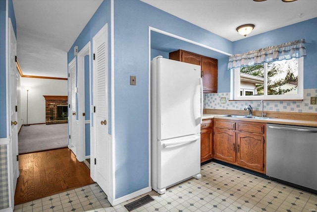 kitchen featuring a fireplace, tasteful backsplash, dishwasher, sink, and white fridge