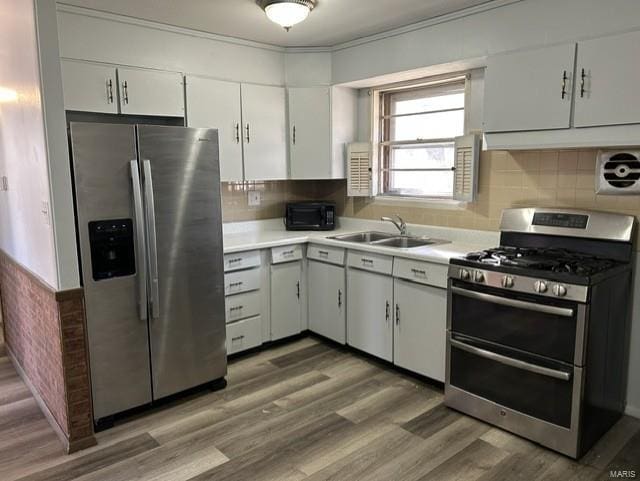 kitchen with sink, hardwood / wood-style floors, stainless steel appliances, tasteful backsplash, and white cabinets