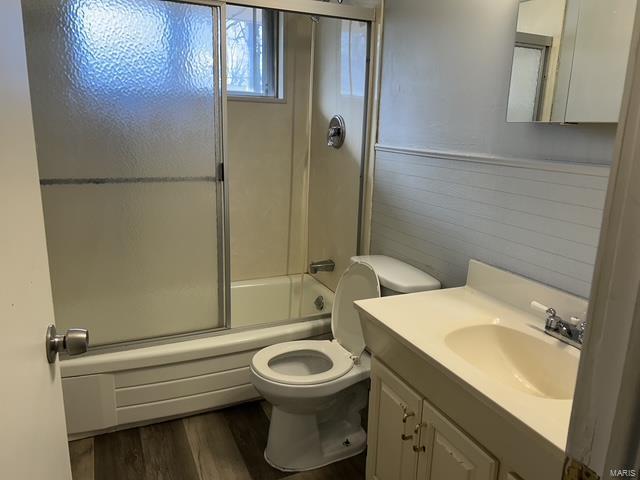 full bathroom with hardwood / wood-style flooring, bath / shower combo with glass door, vanity, and toilet