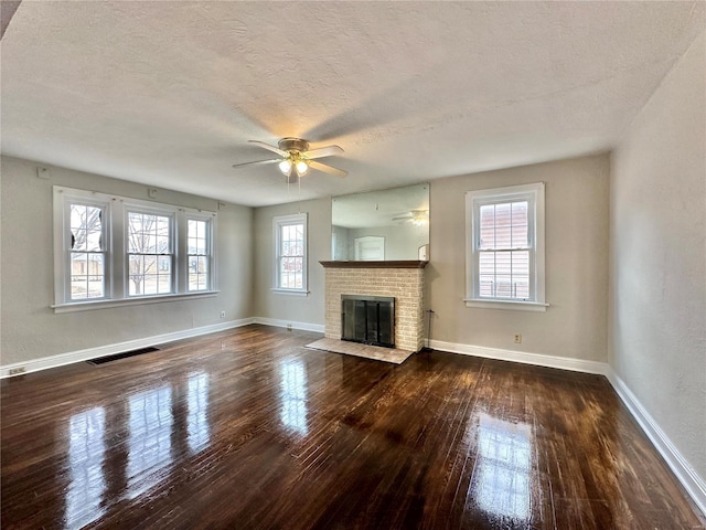 unfurnished living room with a wealth of natural light, a fireplace, dark wood finished floors, and visible vents