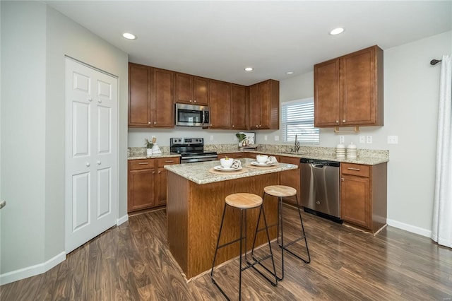 kitchen with baseboards, appliances with stainless steel finishes, dark wood-type flooring, a center island, and a sink