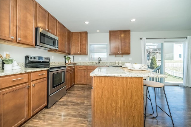 kitchen featuring a kitchen breakfast bar, dark wood-style flooring, a center island, stainless steel appliances, and a sink