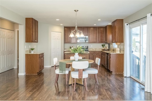 kitchen featuring brown cabinetry, dark wood-style flooring, a sink, stainless steel appliances, and a notable chandelier