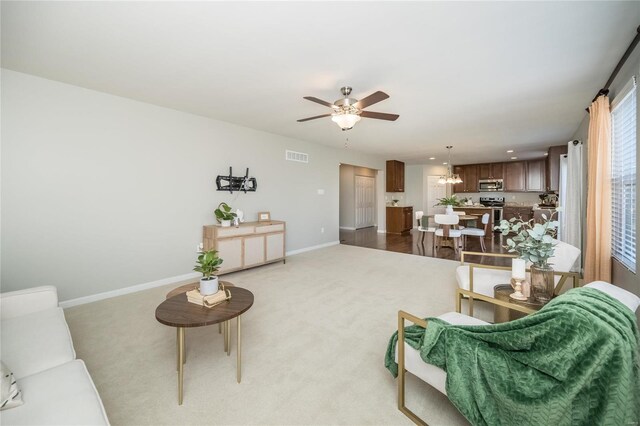 living room with light colored carpet, visible vents, ceiling fan, and baseboards