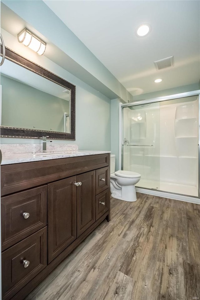 bathroom featuring a stall shower, visible vents, toilet, wood finished floors, and vanity