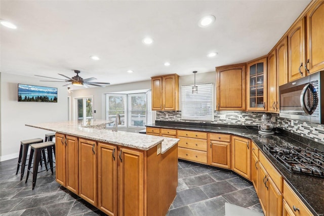 kitchen with tasteful backsplash, decorative light fixtures, a center island with sink, dark stone countertops, and black gas stovetop