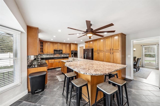 kitchen with sink, a kitchen breakfast bar, black appliances, an island with sink, and decorative backsplash