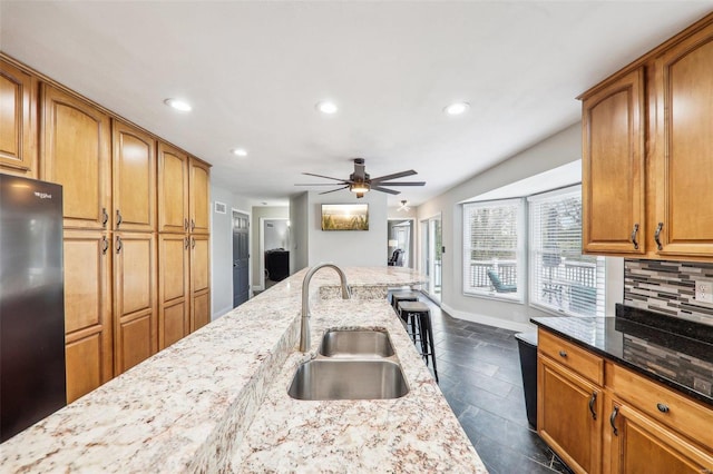 kitchen with sink, ceiling fan, refrigerator, light stone counters, and decorative backsplash