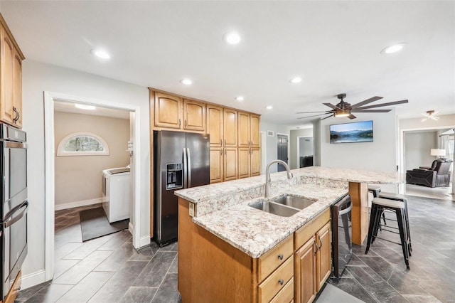 kitchen with a breakfast bar, sink, a kitchen island with sink, independent washer and dryer, and stainless steel appliances