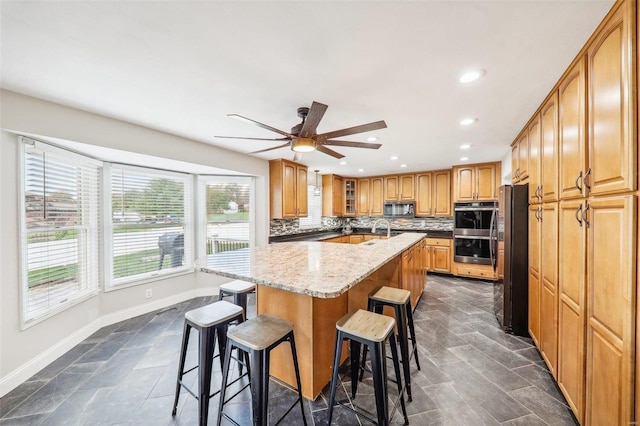 kitchen featuring appliances with stainless steel finishes, a kitchen breakfast bar, decorative backsplash, light stone countertops, and a center island with sink