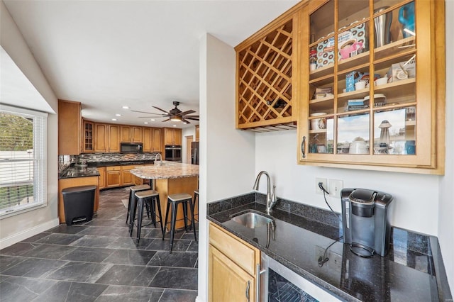 kitchen with sink, stainless steel appliances, a kitchen bar, decorative backsplash, and dark stone counters