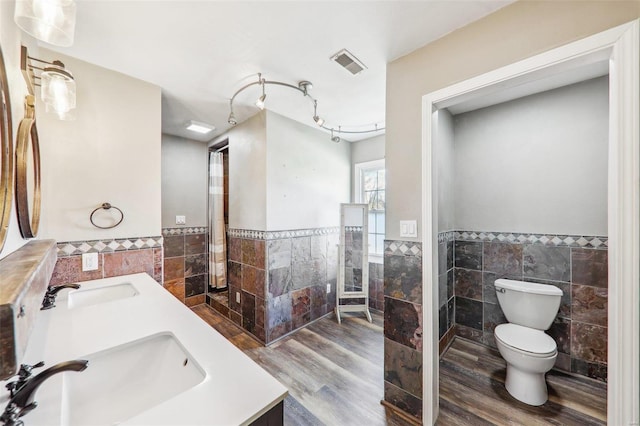 bathroom featuring wood-type flooring, tile walls, vanity, walk in shower, and toilet