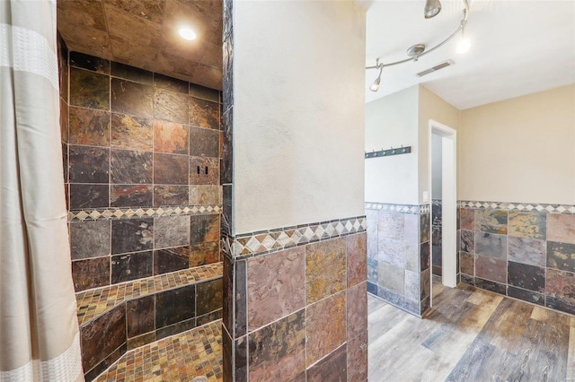 bathroom featuring wood-type flooring, rail lighting, tile walls, and walk in shower