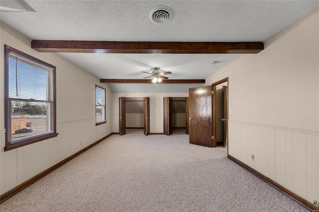 unfurnished bedroom with beam ceiling, light colored carpet, and a textured ceiling