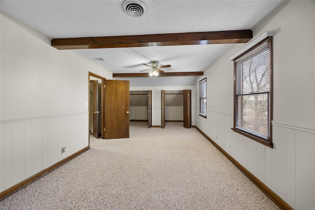 empty room with ceiling fan, beam ceiling, light colored carpet, and a textured ceiling