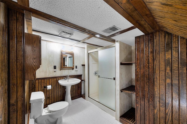 bathroom featuring toilet, sink, wooden walls, and a shower with shower door