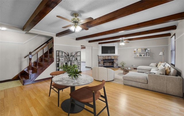 dining room featuring ceiling fan, beam ceiling, light hardwood / wood-style floors, a textured ceiling, and a stone fireplace