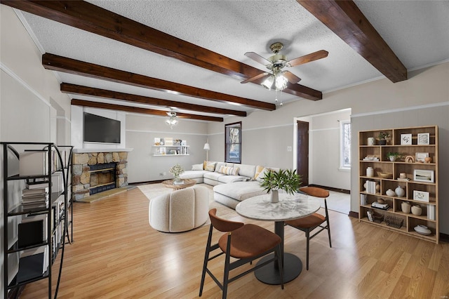 dining area featuring a stone fireplace, beamed ceiling, ceiling fan, light hardwood / wood-style floors, and a textured ceiling