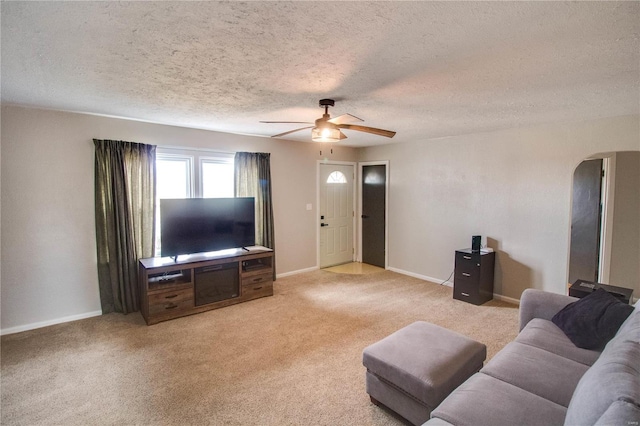 living area with arched walkways, light colored carpet, a ceiling fan, a textured ceiling, and baseboards