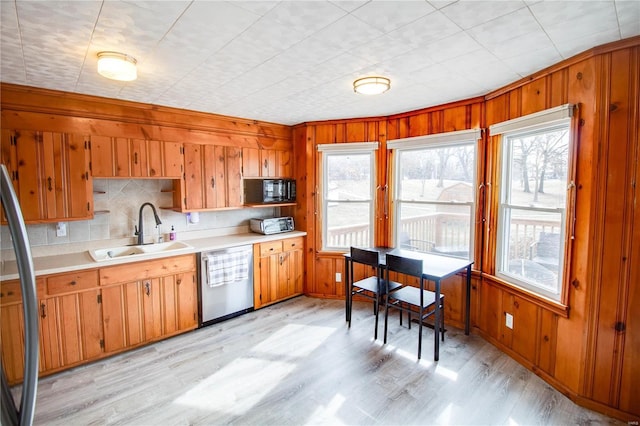 kitchen featuring a sink, light wood-style floors, light countertops, stainless steel dishwasher, and brown cabinets