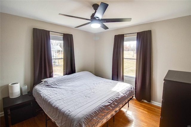 bedroom featuring ceiling fan, multiple windows, wood finished floors, and baseboards