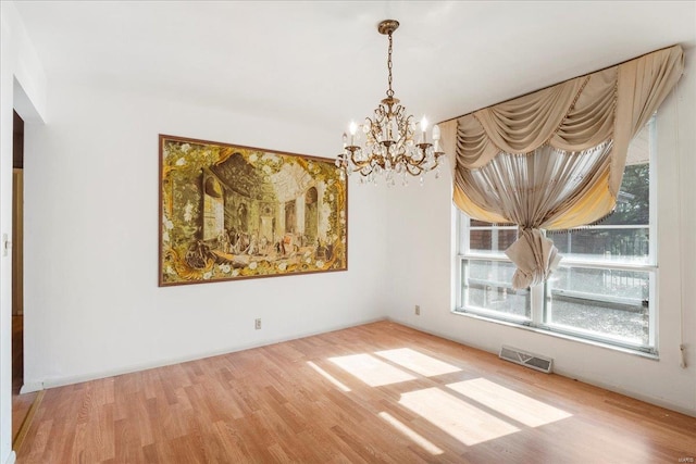 unfurnished dining area featuring visible vents, an inviting chandelier, and wood finished floors