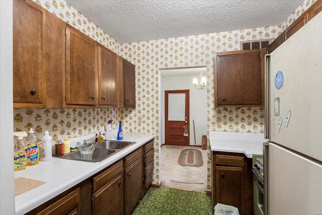 kitchen with a textured ceiling, a sink, freestanding refrigerator, and wallpapered walls