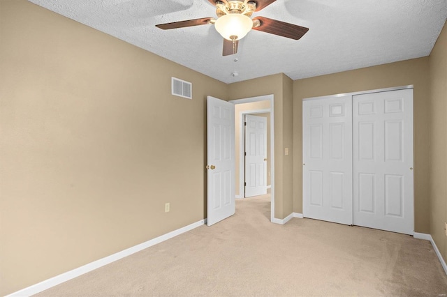 unfurnished bedroom featuring ceiling fan, light colored carpet, a closet, and a textured ceiling