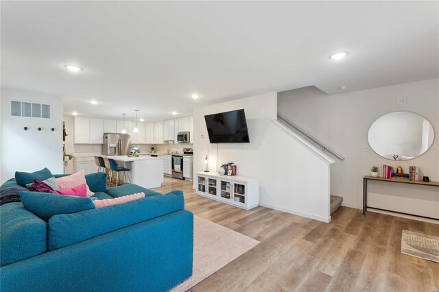 living room with recessed lighting, visible vents, baseboards, stairs, and light wood-style floors