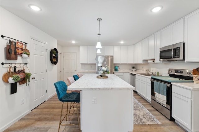 kitchen with appliances with stainless steel finishes, light wood-type flooring, a kitchen island, and a breakfast bar