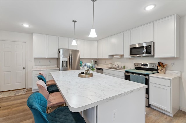 kitchen with stainless steel appliances, a sink, white cabinets, a kitchen breakfast bar, and light countertops