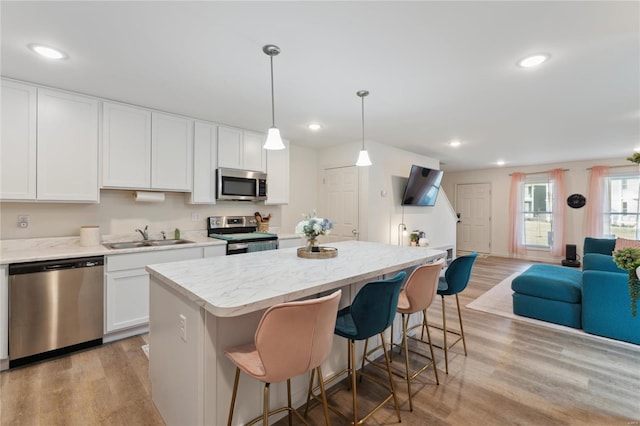 kitchen featuring open floor plan, a center island, stainless steel appliances, light wood-style floors, and a sink