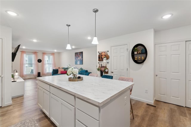 kitchen with decorative light fixtures, light wood-style flooring, open floor plan, white cabinets, and a kitchen island