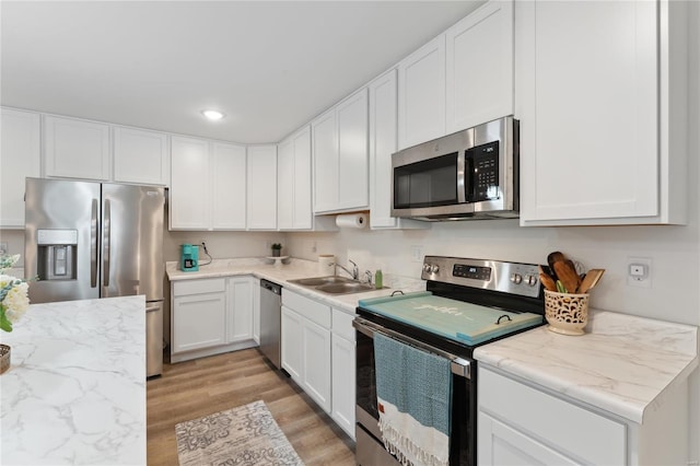 kitchen featuring appliances with stainless steel finishes, light wood-type flooring, white cabinets, and a sink