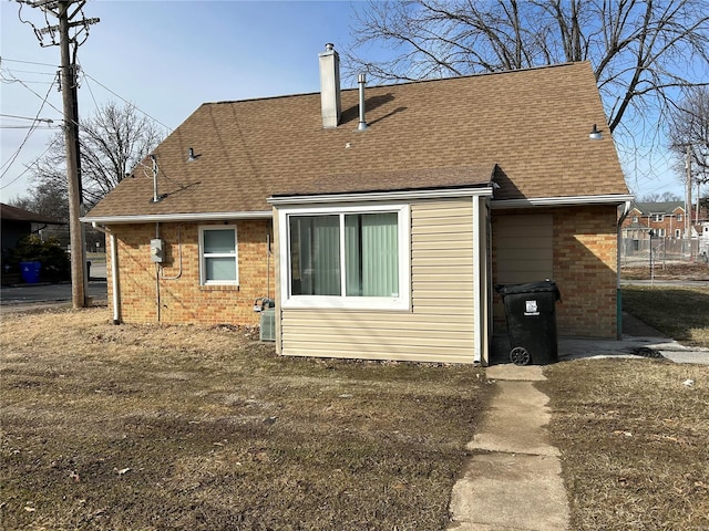 back of property with roof with shingles, a chimney, and brick siding