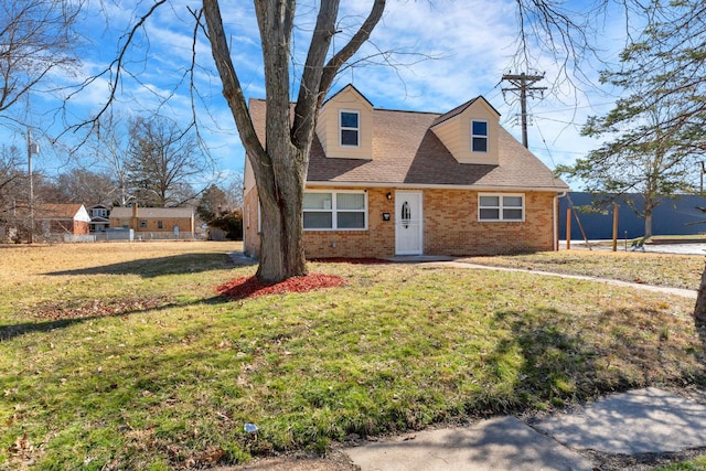 cape cod-style house with a shingled roof, a front yard, and brick siding