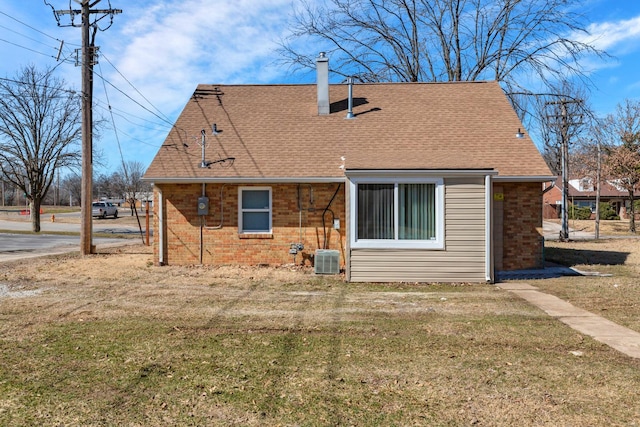 rear view of property featuring cooling unit, brick siding, a shingled roof, a yard, and a chimney