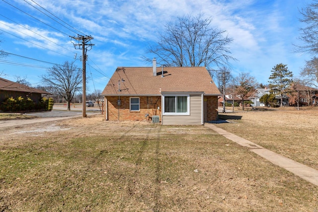 back of house with a shingled roof, a lawn, and brick siding