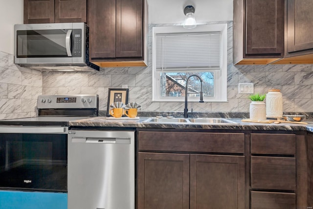 kitchen with dark brown cabinetry, a sink, appliances with stainless steel finishes, tasteful backsplash, and dark stone countertops