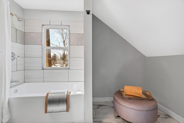 full bath featuring marble finish floor, a bathing tub, baseboards, and vaulted ceiling