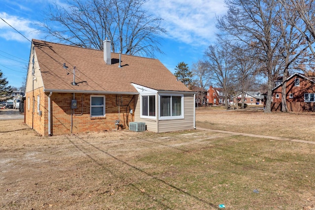 back of property with central AC, brick siding, a yard, roof with shingles, and a chimney