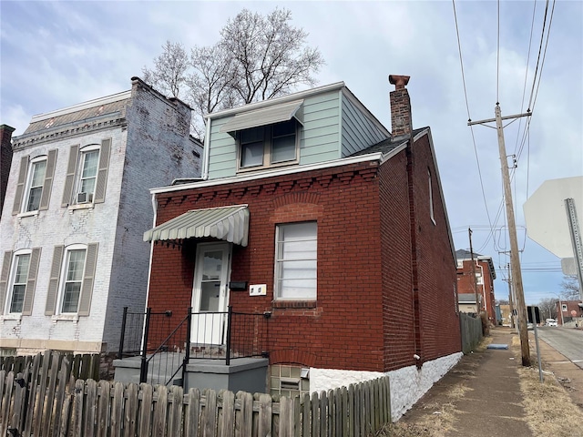 view of front of home with fence, brick siding, and a chimney